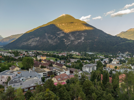 Aerial view of the town of Imst nestled in a lush mountain valley with historic buildings and dense forest under a clear sky in Imst Tyrol Austria.