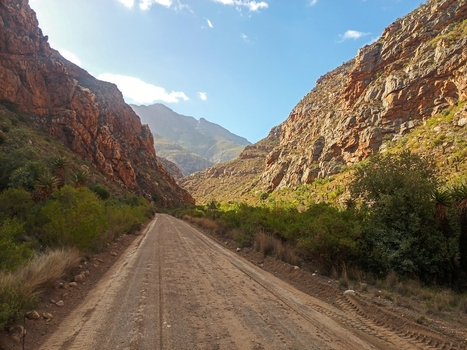 View of a dirt road winding through the rugged rock formations and mountain pass of the Klein Karoo with native shrubs and a clear blue sky in Robertson Western Cape South Africa. View of a dirt road winding through the rugged rock formations and mountain pass of the Klein Karoo with native shrubs and a clear blue sky in Robertson Western Cape South Africa.