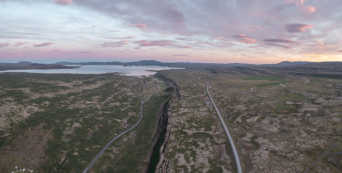 Aerial view of the tectonic rift valley at Thingvellir National Park with mossy lava fields a winding road and a distant lake under a sunset sky in Selfoss Blaskogabyggd Iceland. Aerial view of the tectonic rift valley at Thingvellir National Park with mossy lava fields a winding road and a distant lake under a sunset sky in Selfoss Blaskogabyggd Iceland.