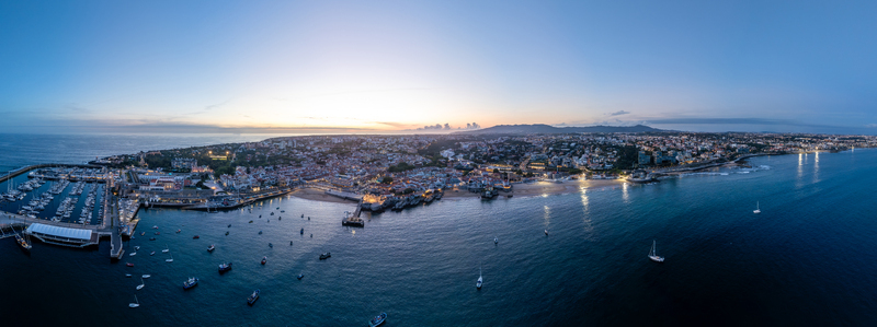 Aerial view of the illuminated coastline marina with yachts and sandy beaches at twilight under a clear sky in Cascais Lisbon Portugal.