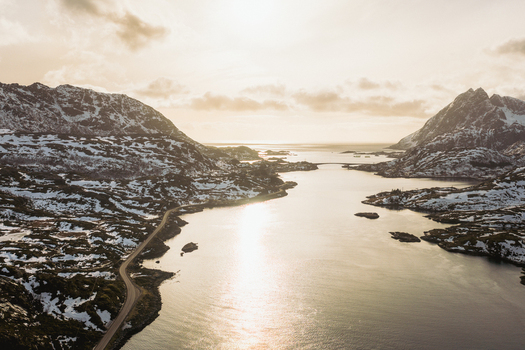 Aerial view of snowy mountains embracing the serene waters reflecting the golden sunlight near Kåkernbrua bridge Kåkernbrua Nordland Norway. Aerial view of snowy mountains embracing the serene waters reflecting the golden sunlight near Kåkernbrua bridge Kåkernbrua Nordland Norway.