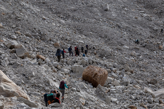 View of hikers trekking across the rocky terrain of the Baltoro Glacier with large boulders and mountain slopes in the background in Baltoro Gilgit Baltistan Pakistan.