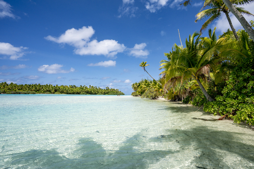View of the pristine turquoise waters and sandy shores of One Foot Island in Aitutaki with lush palm trees under a bright blue sky in Arutanga Cook Islands. View of the pristine turquoise waters and sandy shores of One Foot Island in Aitutaki with lush palm trees under a bright blue sky in Arutanga Cook Islands.