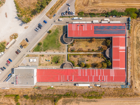 Aerial view of an industrial facility featuring large red roofs with solar panels a parking lot with vehicles and surrounding dry fields in Gelemenovo Pazardzhik Bulgaria. Aerial view of an industrial facility featuring large red roofs with solar panels a parking lot with vehicles and surrounding dry fields in Gelemenovo Pazardzhik Bulgaria.