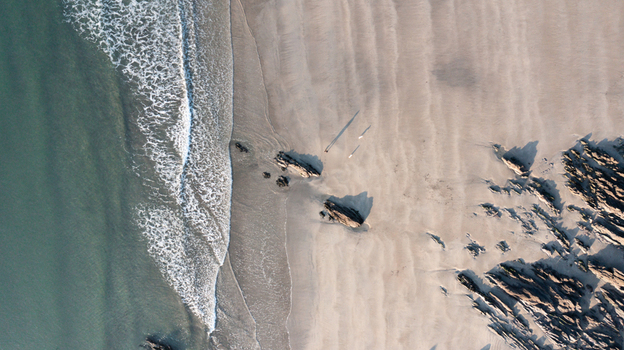 Aerial view of two people walking on the sandy shore of Mothecombe Beach with waves crashing against rocks and casting long shadows Mothecombe Devon United Kingdom. Aerial view of two people walking on the sandy shore of Mothecombe Beach with waves crashing against rocks and casting long shadows Mothecombe Devon United Kingdom.