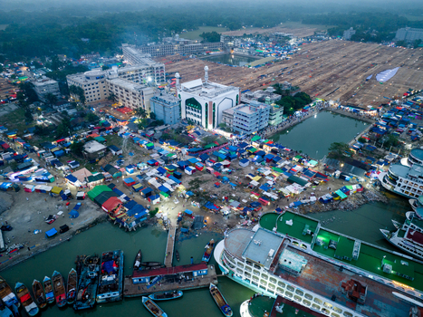 Aerial view of a bustling waterfront with boats docked near tents and buildings a mosque rising amidst the lively scene Charmonai Barisal Division Bangladesh. Aerial view of a bustling waterfront with boats docked near tents and buildings a mosque rising amidst the lively scene Charmonai Barisal Division Bangladesh.
