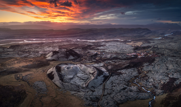Aerial view of volcanic craters in a vast lava field under a dramatic sunset sky with orange clouds in Iceland.
