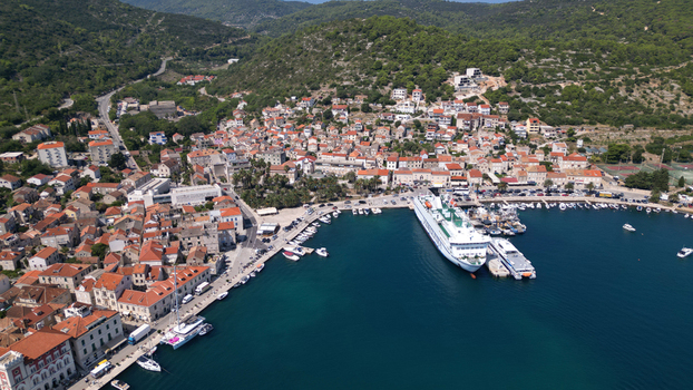 Aerial view of Vis town harbor with a large white ferry docked near red roofed houses and lush green hills in Vis Split Dalmatia County Croatia. Aerial view of Vis town harbor with a large white ferry docked near red roofed houses and lush green hills in Vis Split Dalmatia County Croatia.