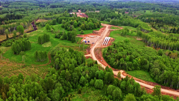 Aerial view of a wind turbine maintenance road under construction through a lush green forest with large turbine blades resting on the ground in Latvia. Aerial view of a wind turbine maintenance road under construction through a lush green forest with large turbine blades resting on the ground in Latvia.
