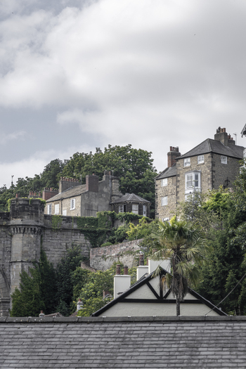 View of historic stone buildings and a stone fortification wall surrounded by lush greenery and trees in Knaresborough England United Kingdom.