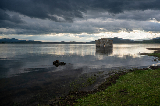 View of the submerged Church of St. John of Rila in the Zhrebchevo Reservoir under a dramatic dark cloudy sky with soft light reflecting on the water surface in Sliven Bulgaria. View of the submerged Church of St. John of Rila in the Zhrebchevo Reservoir under a dramatic dark cloudy sky with soft light reflecting on the water surface in Sliven Bulgaria.