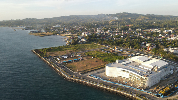 Aerial view of a large modern building under construction along the waterfront with urban development and hills in the background Sorong Southwest Papua Indonesia. Aerial view of a large modern building under construction along the waterfront with urban development and hills in the background Sorong Southwest Papua Indonesia.