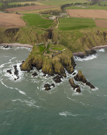 Aerial view of Dunnottar Castle ruins on a dramatic rocky headland with crashing waves and green coastal fields Stonehaven Scotland United Kingdom. Aerial view of Dunnottar Castle ruins on a dramatic rocky headland with crashing waves and green coastal fields Stonehaven Scotland United Kingdom.