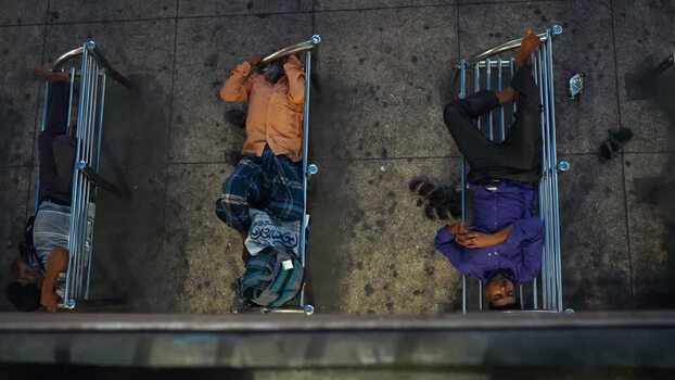 View of men sleeping on metal benches in a public space Bangladesh.