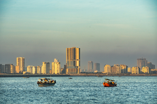View of the Karachi skyline with modern high rise buildings along the coastline and small fishing boats sailing on the water in Karachi Sindh Pakistan.