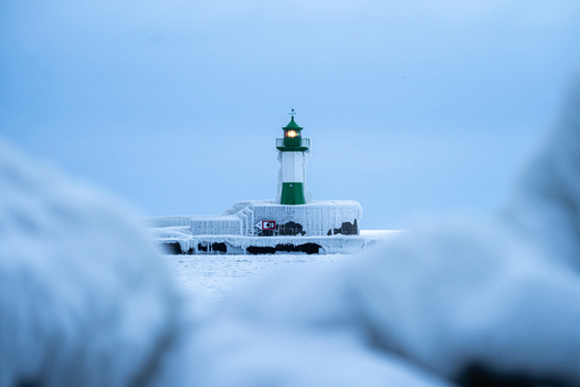 View of the ice covered Molenfeuer Sassnitz lighthouse surrounded by frozen structures and a calm sea during a cold winter day in Sassnitz Mecklenburg Vorpommern Germany.