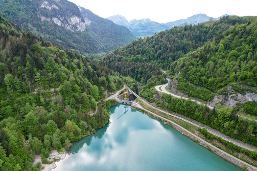 Aerial view of Lac du Vernex surrounded by dense green forests steep mountain slopes and a dam structure in Rossiniere Vaud Switzerland.