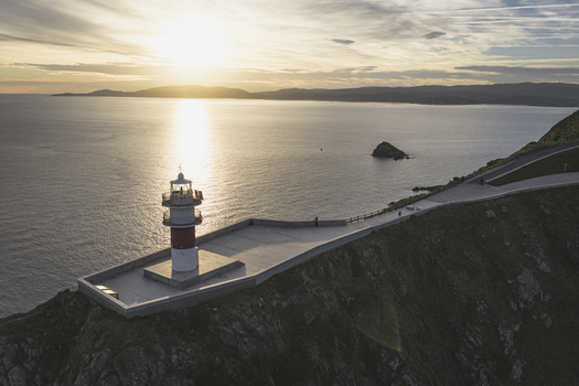 Aerial view of a lighthouse on a rocky cliff overlooking the ocean at sunset in Galicia Spain.