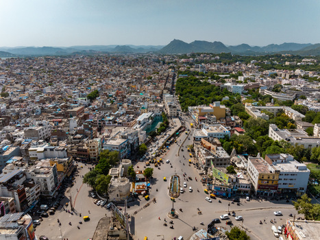 Aerial view of the dense urban landscape featuring historic buildings busy streets with traffic and surrounding hills under a clear sky in Udaipur Rajasthan India.