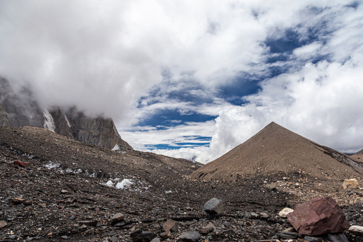 View of the rugged landscape of Baltoro Glacier with its rocky moraine a prominent pyramid shaped mountain peak and dramatic clouds in Baltoro Gilgit Baltistan Pakistan.