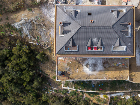 Aerial view of a house under construction with a dark tiled roof and dormer windows featuring an excavator on the dirt ground surrounded by trees in Istanbul Istanbul Turkiye.