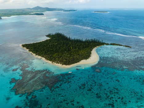 Aerial view of a lush verdant islet embraced by turquoise waters and fringed with white sand contrasting against the deep blue of the open ocean Noumea New Caledonia. Aerial view of a lush verdant islet embraced by turquoise waters and fringed with white sand contrasting against the deep blue of the open ocean Noumea New Caledonia.