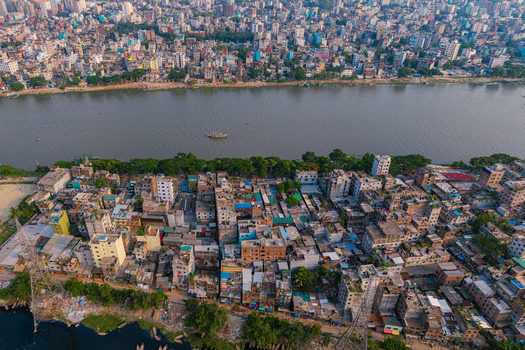 Aerial view of the Buriganga River flowing through dense urban neighborhoods with colorful rooftops and small boats in Keraniganj Dhaka Division Bangladesh. Aerial view of the Buriganga River flowing through dense urban neighborhoods with colorful rooftops and small boats in Keraniganj Dhaka Division Bangladesh.