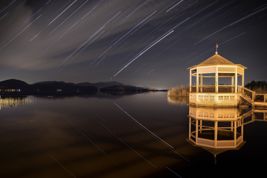 View of Lago di Massaciuccoli with a wooden gazebo and star trails reflecting in the calm water Province of Lucca Tuscany Italy.