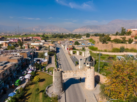 Aerial view of the historic Khyber Pass gate spanning the road with surrounding urban buildings lush greenery and distant mountains in Khyber District Khyber Pakhtunkhwa Pakistan. Aerial view of the historic Khyber Pass gate spanning the road with surrounding urban buildings lush greenery and distant mountains in Khyber District Khyber Pakhtunkhwa Pakistan.
