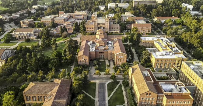 Aerial view of the UCLA campus featuring historic red brick buildings with terracotta roofs lush green trees and manicured lawns in Westwood California United States.