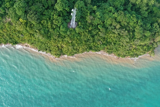 Aerial view of a communication tower standing amidst dense tropical vegetation on the coastline of Pulau Maginti with turquoise waters meeting the shore in Maginti South East Sulawesi Indonesia.