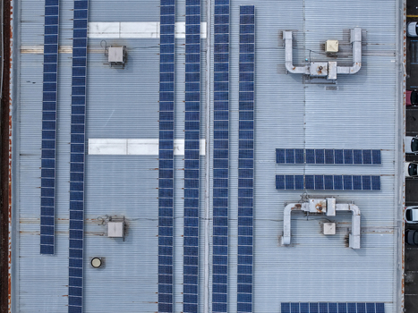 Aerial view of solar panel arrays installed on a corrugated metal industrial roof with HVAC ventilation units in Melbourne VIC Australia.