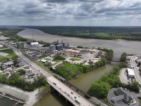 Aerial view of the Ohio River featuring industrial silos a road bridge with traffic and lush green riverbanks under a cloudy sky in Aurora Indiana United States. Aerial view of the Ohio River featuring industrial silos a road bridge with traffic and lush green riverbanks under a cloudy sky in Aurora Indiana United States.