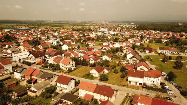 Aerial view of a residential neighborhood with houses featuring red tiled roofs surrounded by green lawns and trees in Croatia.