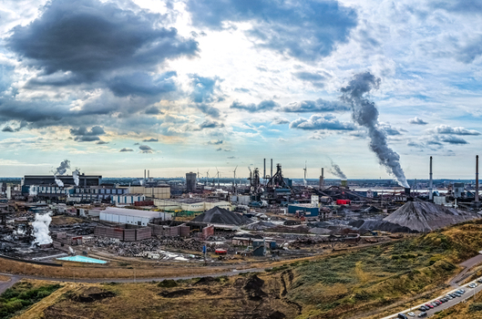 Aerial view of Tata Steel industrial complex with smokestacks emitting steam raw material piles and infrastructure under a cloudy sky in Velsen Noord Noord Holland Netherlands. Aerial view of Tata Steel industrial complex with smokestacks emitting steam raw material piles and infrastructure under a cloudy sky in Velsen Noord Noord Holland Netherlands.