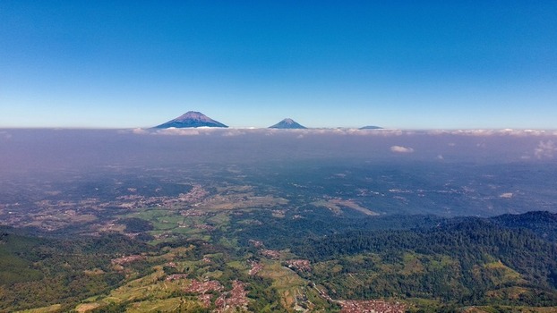 Aerial view of Mount Sindoro and Mount Sumbing rising above a sea of clouds over the lush rural landscape of Pringsurat Central Java Indonesia.
