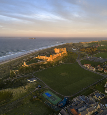 Aerial view of Bamburgh Castle on a rocky outcrop overlooking the North Sea coast and sandy beach during sunset Bamburgh England United Kingdom. Aerial view of Bamburgh Castle on a rocky outcrop overlooking the North Sea coast and sandy beach during sunset Bamburgh England United Kingdom.