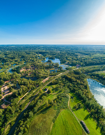 Aerial view of a lush landscape featuring dense forests a winding river and open green fields under a clear blue sky Latvia. Aerial view of a lush landscape featuring dense forests a winding river and open green fields under a clear blue sky Latvia.