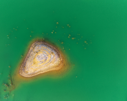Aerial view of the unique concentric rock formations of a small island surrounded by vibrant emerald green water at the mining site Minas de Riotinto Andalusia Spain.