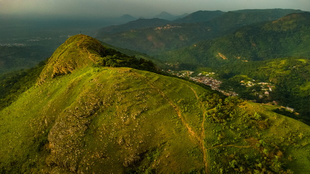 Aerial view of Mt. Gemi with its lush green slopes rugged terrain and a small village nestled in the valley below under soft light in Amedzofe Volta Region Ghana. Aerial view of Mt. Gemi with its lush green slopes rugged terrain and a small village nestled in the valley below under soft light in Amedzofe Volta Region Ghana.