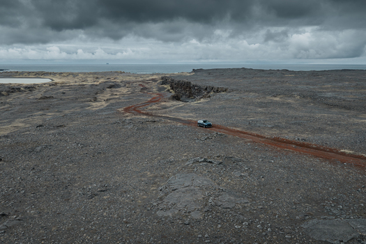 Aerial view of a car driving along a red dirt road through the volcanic landscape near Sandfellshaed Viewpoint in Keflavik Reykjanesbaer Iceland.