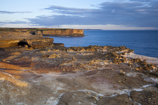 View of Twelve Apostles Marine National Park with rugged limestone cliffs a sea cave and the blue ocean under a soft sky Australia. View of Twelve Apostles Marine National Park with rugged limestone cliffs a sea cave and the blue ocean under a soft sky Australia.