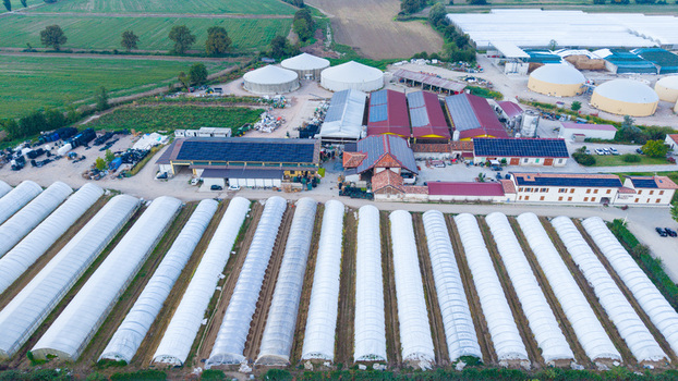Aerial view of a modern farm featuring numerous greenhouses large biogas storage tanks and buildings with solar panels on the roofs situated in the rural landscape of Milan Lombardy Italy. Aerial view of a modern farm featuring numerous greenhouses large biogas storage tanks and buildings with solar panels on the roofs situated in the rural landscape of Milan Lombardy Italy.