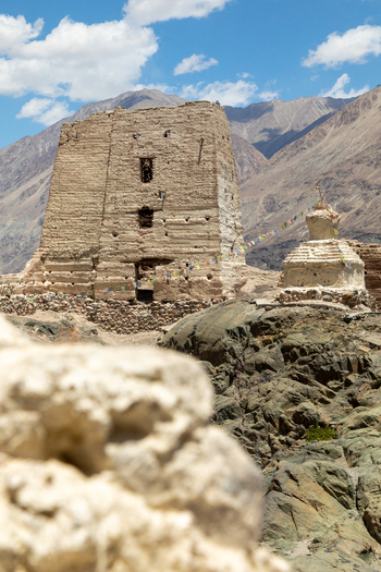 View of the ancient mud brick structure and stupa of Charasa Gonpa adorned with prayer flags against a backdrop of rugged mountains in Charasa Ladakh India.