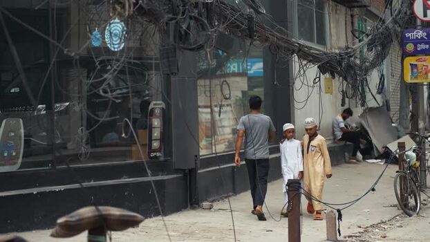 View of people walking past tangled wires in Dhaka Bangladesh.