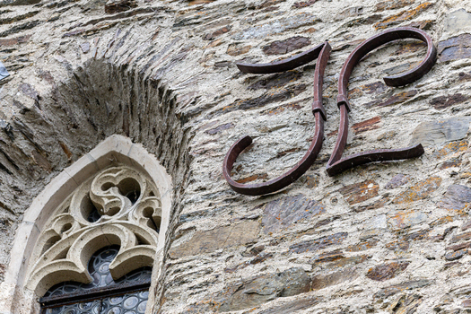 View of the medieval stone wall of Eltz Castle featuring a gothic window with intricate tracery and a decorative wrought iron monogram Wierschem Rhineland Palatinate Germany.