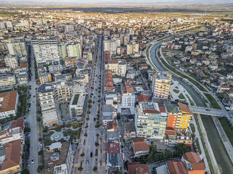 Aerial view of Rruga Jakov Xoxa in the city of Fier featuring urban architecture residential buildings and a canal under golden hour light in Fier Qarku i Fierit Albania.