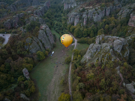 Aerial view of a yellow hot air balloon landing in the Belogradchik Rocks surrounded by lush forest and unique sandstone formations in Belogradchik Vidin Bulgaria.