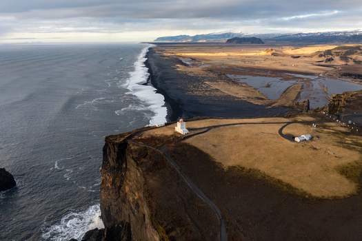 Aerial view of Dyrholaey lighthouse perched on a dramatic cliff edge overlooking the black sand beach and the Atlantic Ocean Myrdalshreppur Iceland. Aerial view of Dyrholaey lighthouse perched on a dramatic cliff edge overlooking the black sand beach and the Atlantic Ocean Myrdalshreppur Iceland.