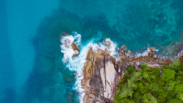 Aerial view of the turquoise ocean waves crashing against the rocky cliffs and lush tropical vegetation at Grand Anse Mahe Seychelles. Aerial view of the turquoise ocean waves crashing against the rocky cliffs and lush tropical vegetation at Grand Anse Mahe Seychelles.